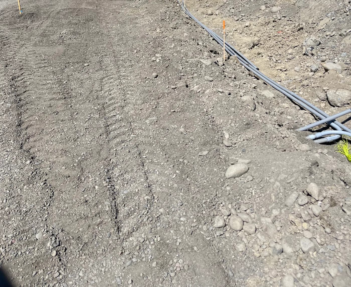 Compacted gravel subgrade graded for a new road with survey stakes along the shoulder