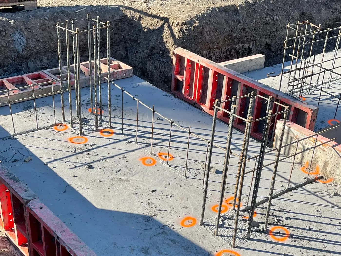 Column dowel clusters rising from a cured slab with orange survey layout marks painted at each location