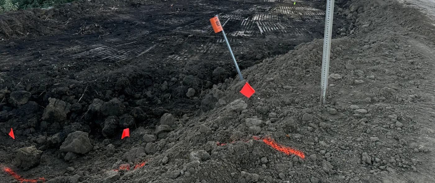 Stripped roadside ditch line with survey flags set for regrading and drainage works