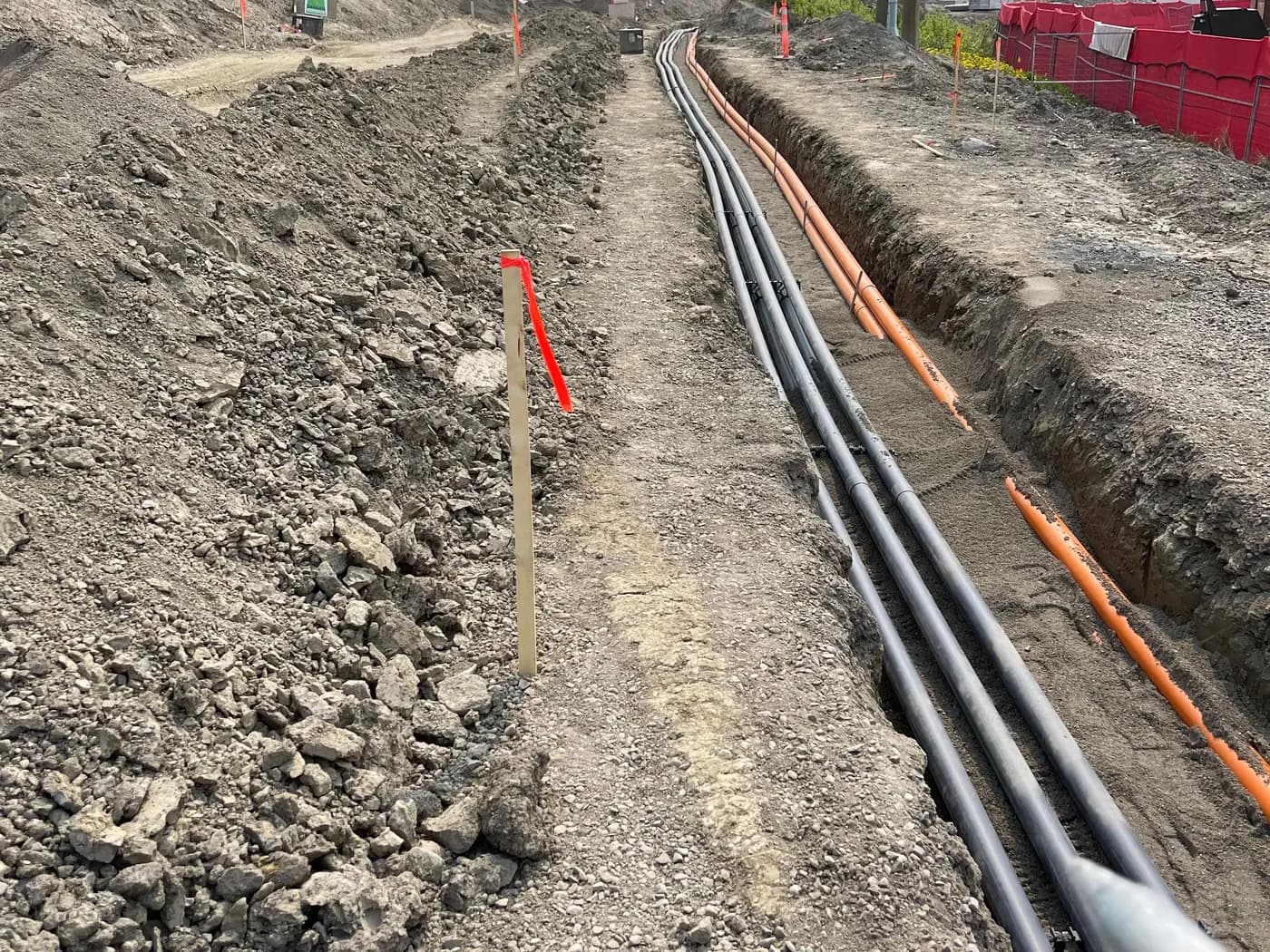 Open trench with multiple conduit runs installed and staked for a utility corridor
