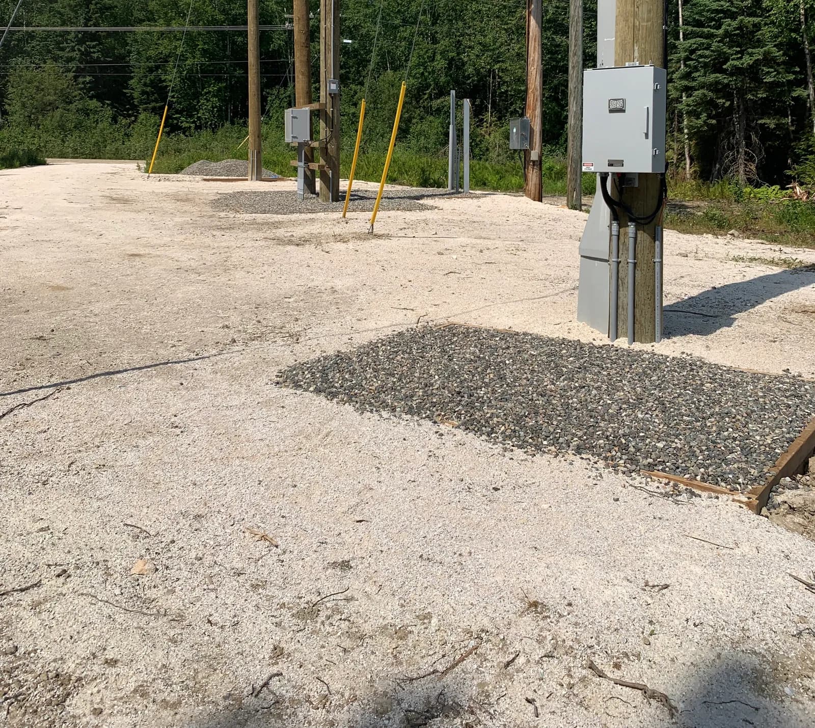 New electrical service pad with a pad-mount kiosk, conduit stub-ups, bollards, and a pole line on a cleared Campbell River site