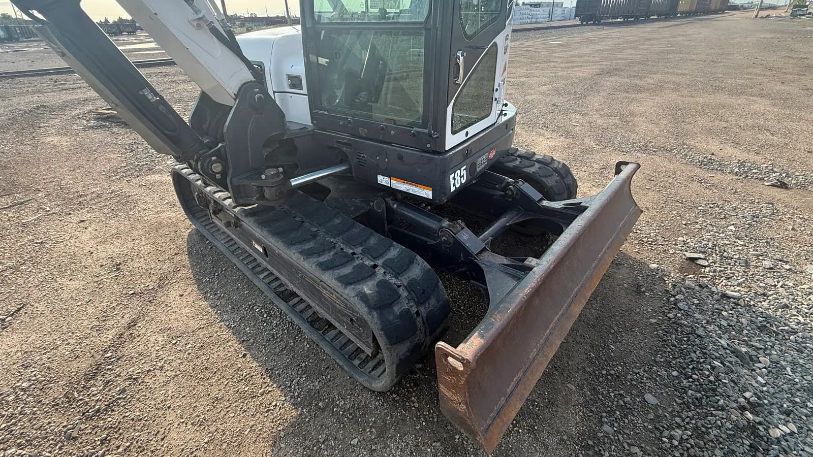 Compact tracked excavator with a dozer blade parked on a prepared gravel pad