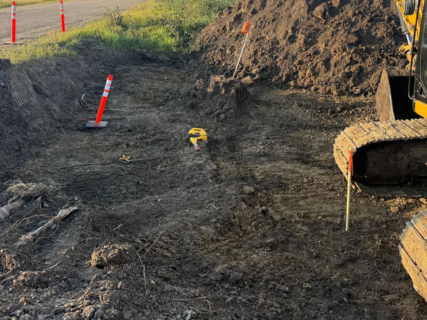 Excavator working beside a marked and staked excavation area with locate cones in place