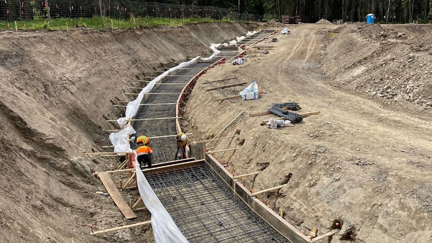 Curved strip footing excavation with rebar and formwork in place and crew working, ready for a foundation pour