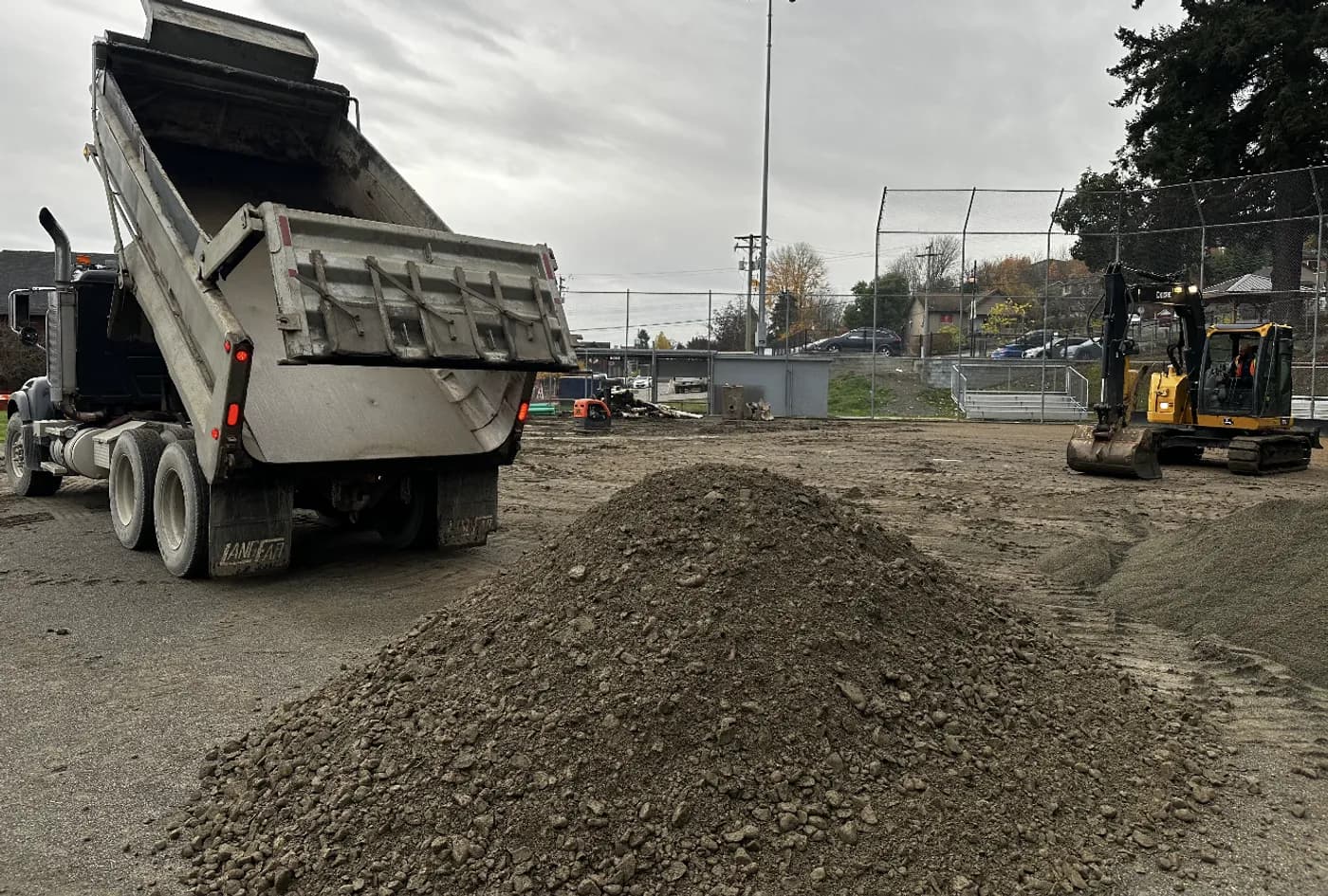 Dump truck delivering crushed granular base beside an excavator for a transformer pad and equipment yard