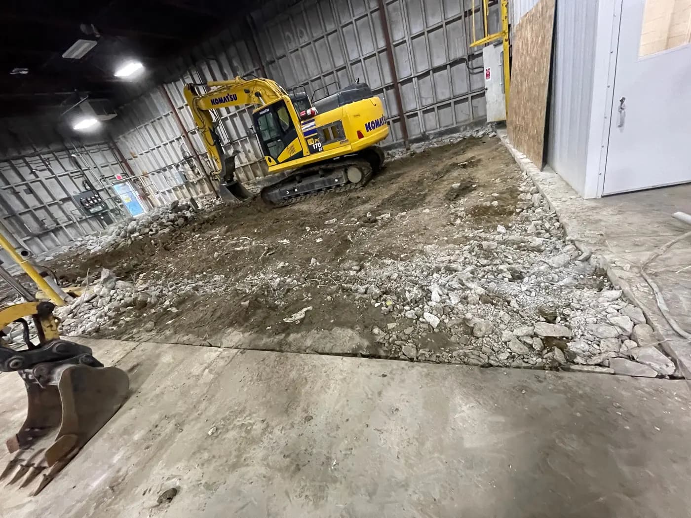 Excavator breaking out and excavating a concrete floor slab inside an industrial building