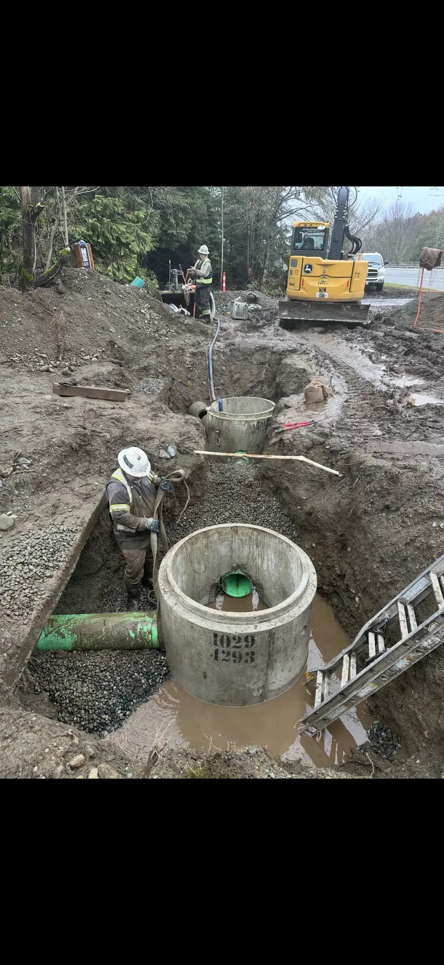 Crew installing a precast concrete manhole in a deep utility trench
