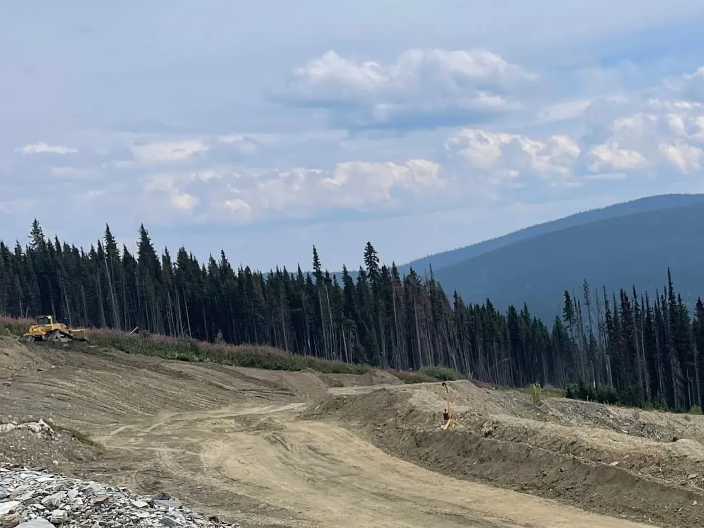 Newly built haul road cut through forested hills below a mountain ridge in Northern BC