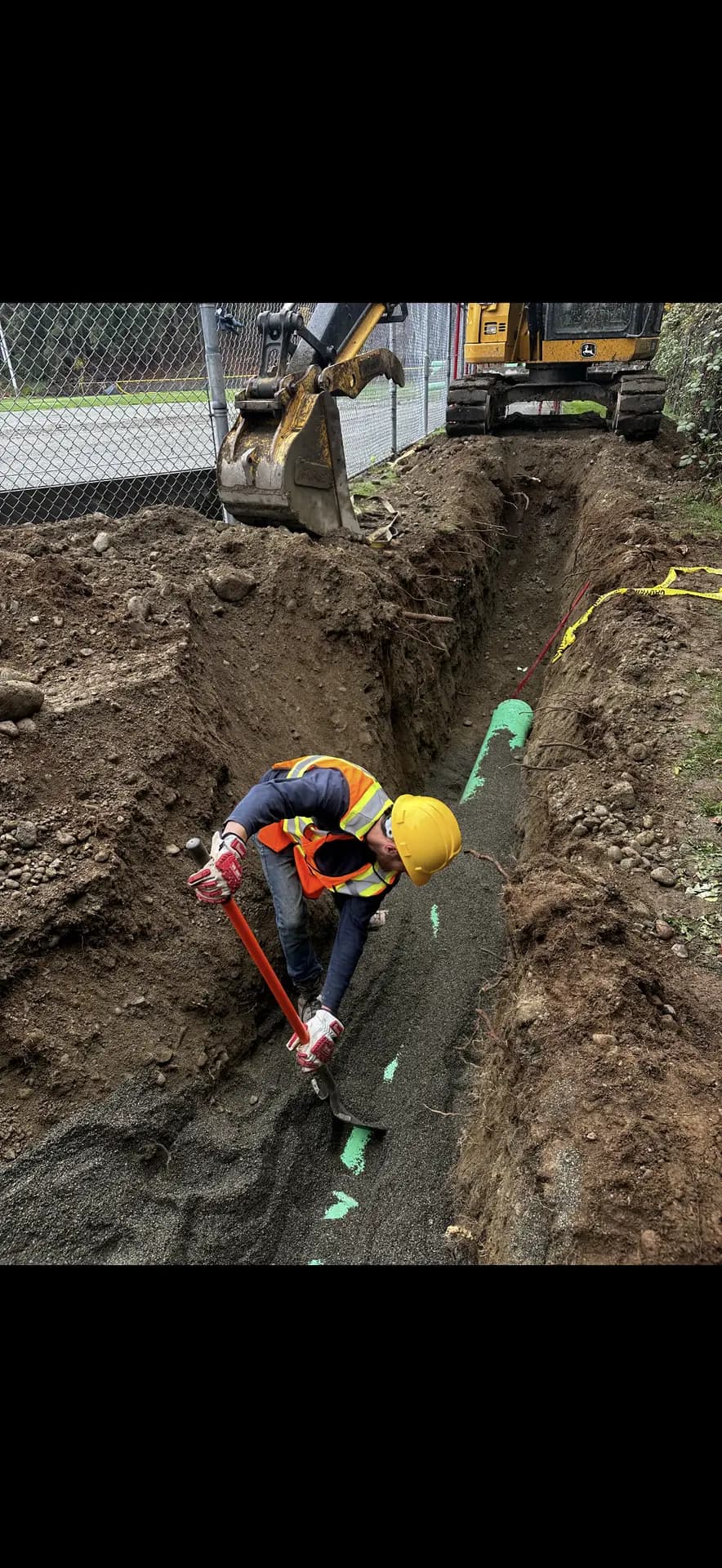 Pipe layer connecting green PVC sewer main in a shored trench