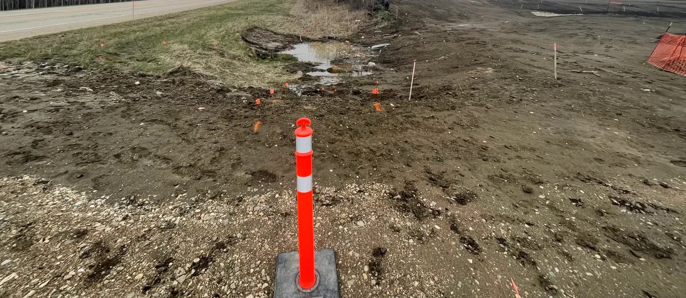Roadside ditch with pooled water and layout stakes ahead of ditching and culvert works