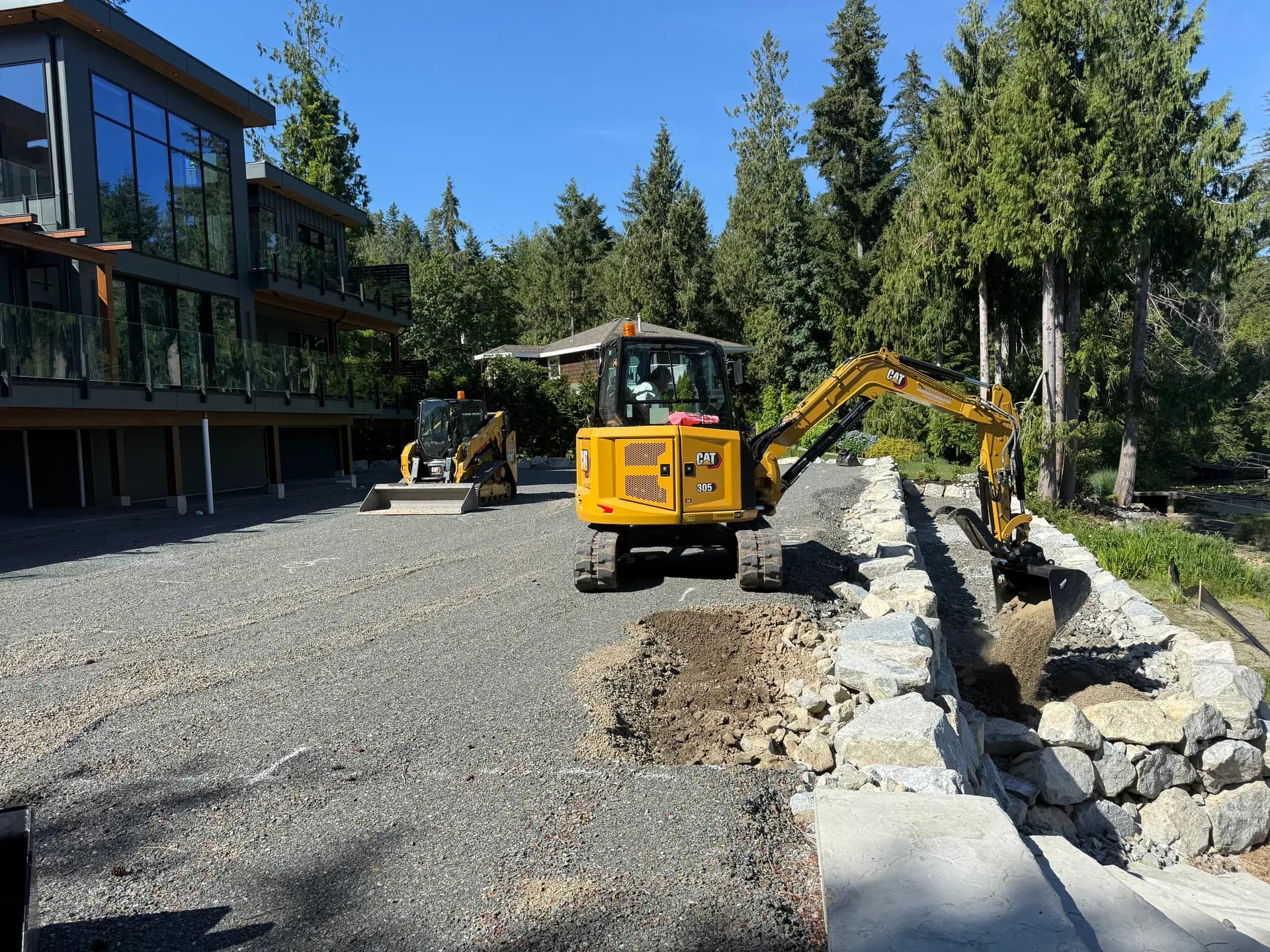 Mini excavator and track loader building a rock retaining wall at a waterfront residence