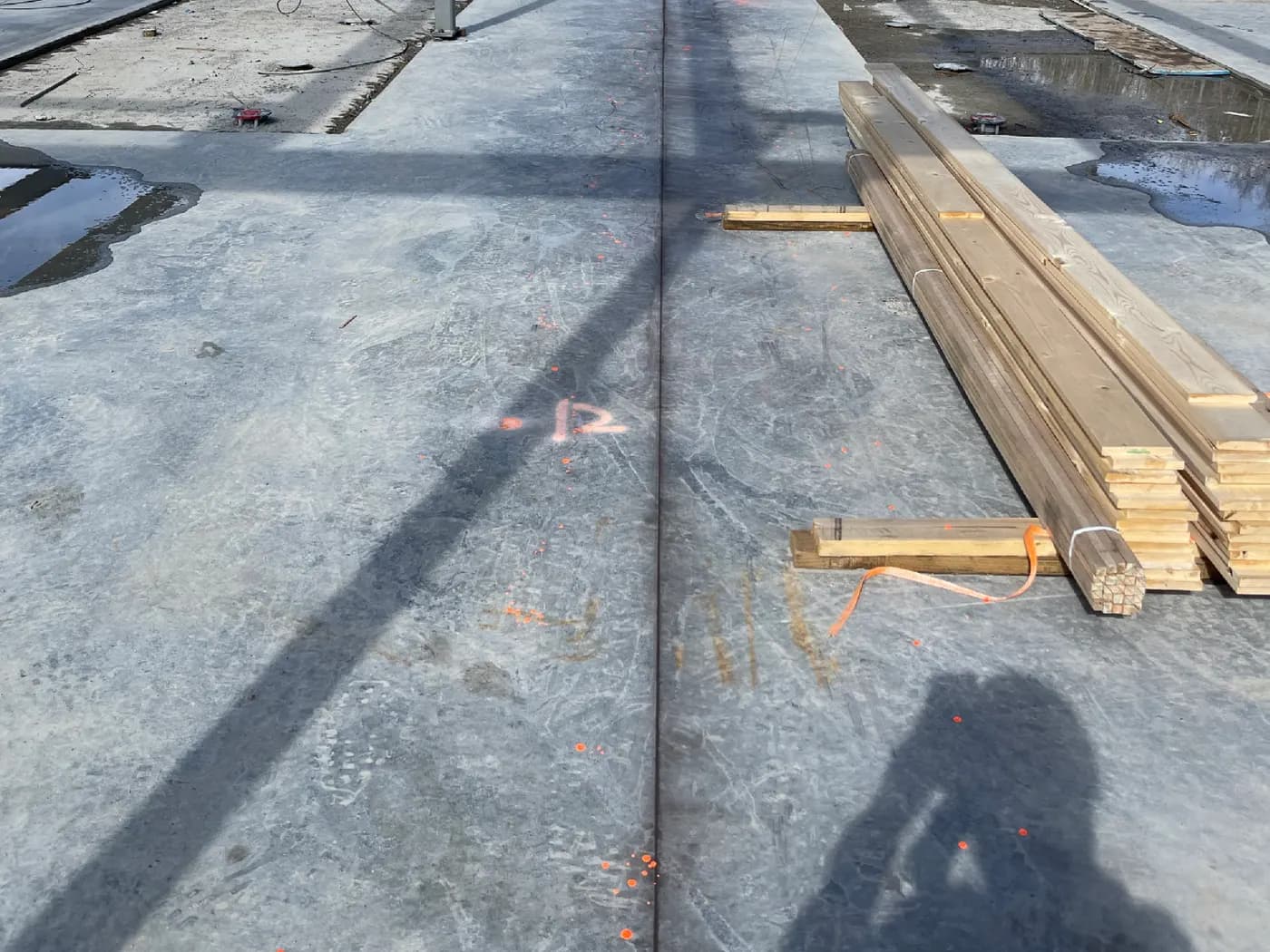 Cured concrete slab with survey layout marks and framing lumber staged for the next phase of construction