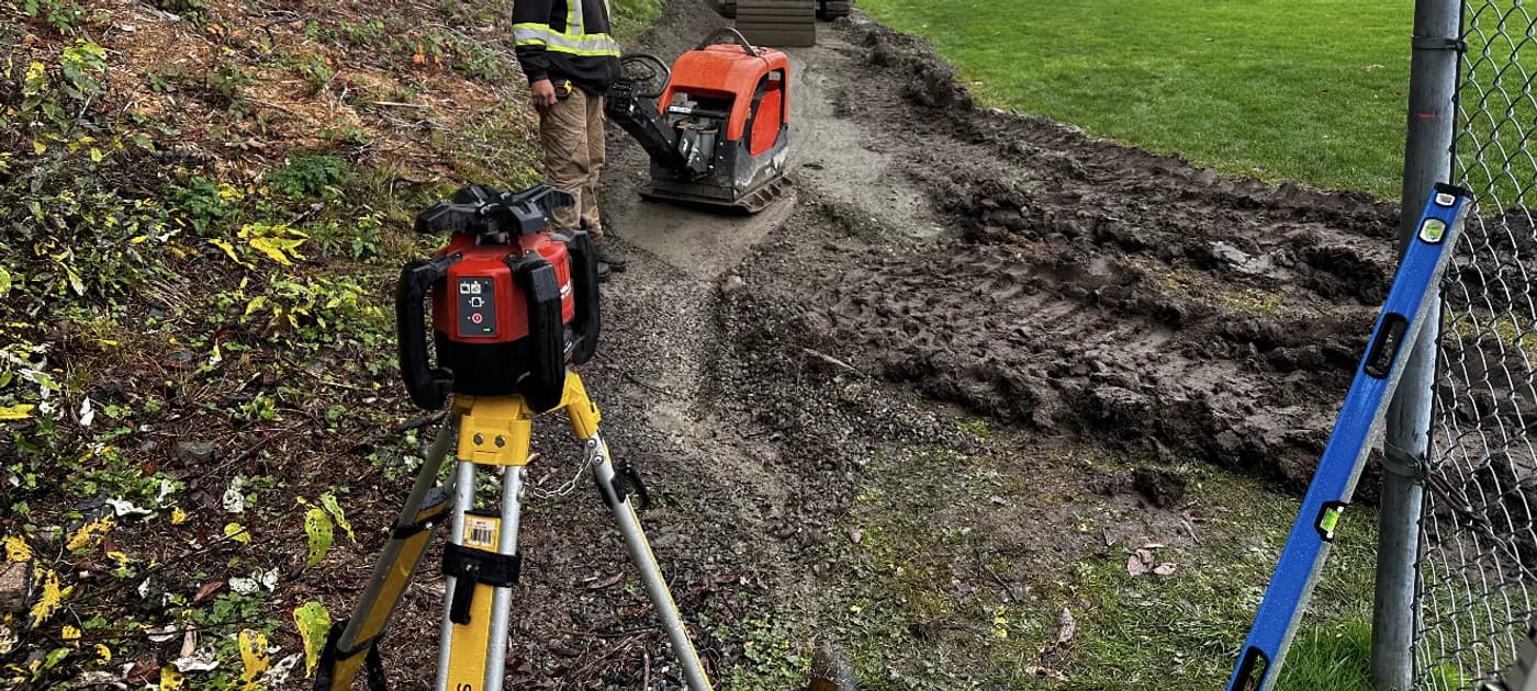 Plate compactor working a backfilled conduit trench with a rotating laser level set for grade control