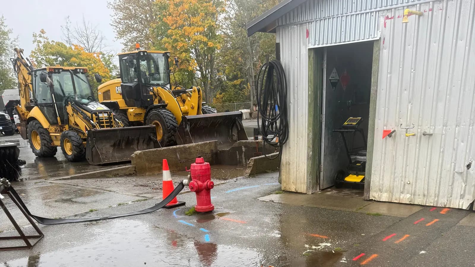 Utility locate paint markings on wet pavement beside a hydrant and construction equipment